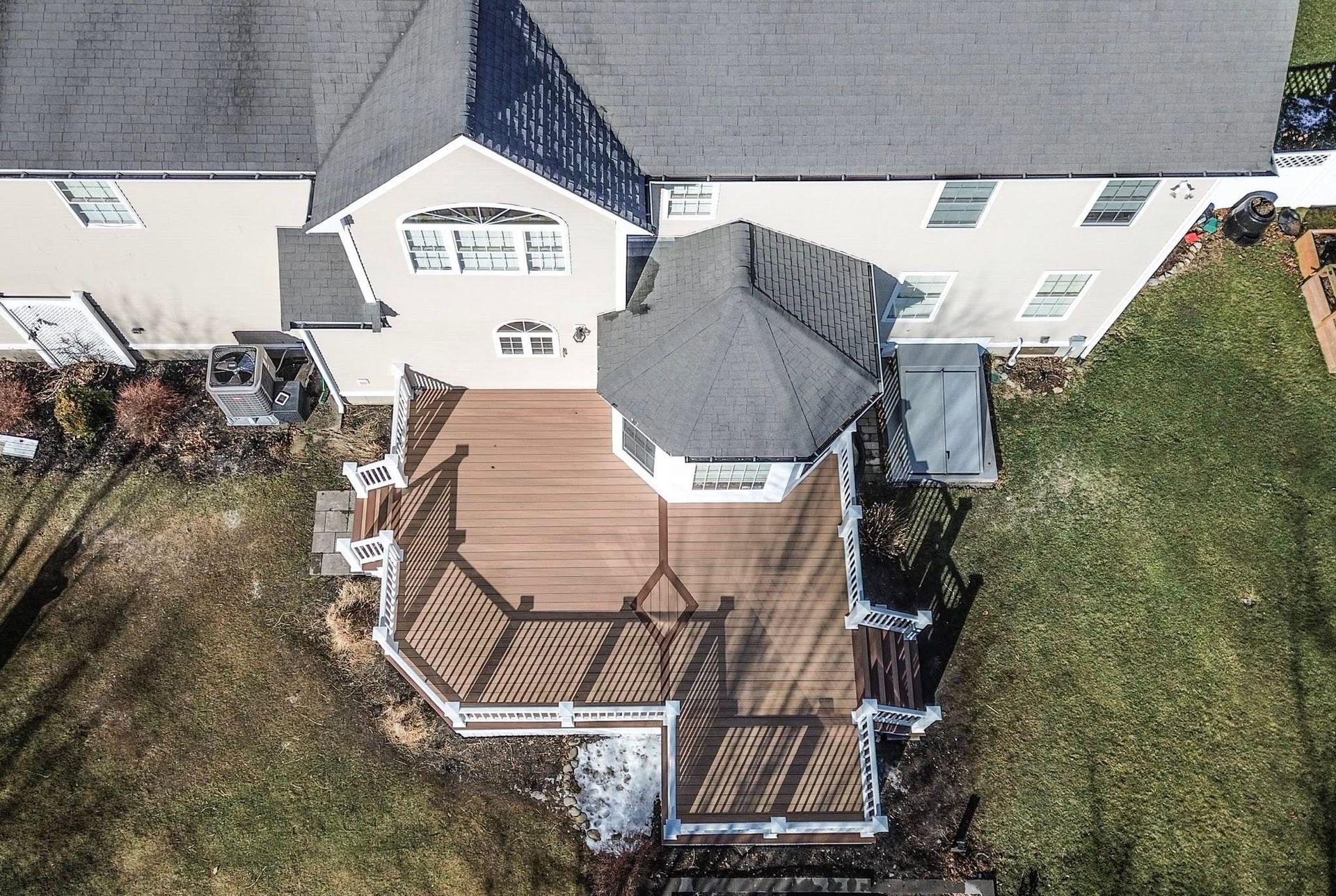 Aerial view of a wooden backyard deck with white railings beside a house and lawn.