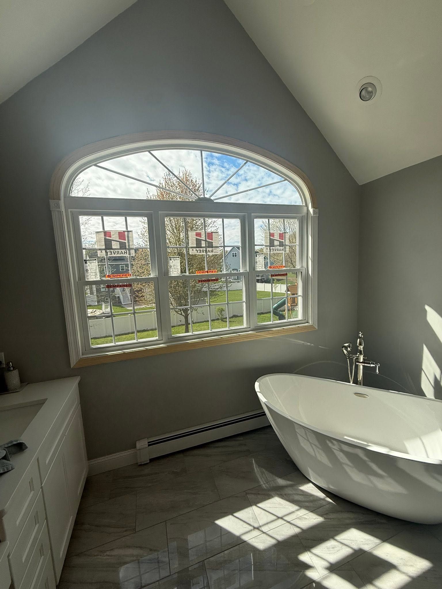 Bright bathroom with arched window, white bathtub, and tiled floor in sunlight