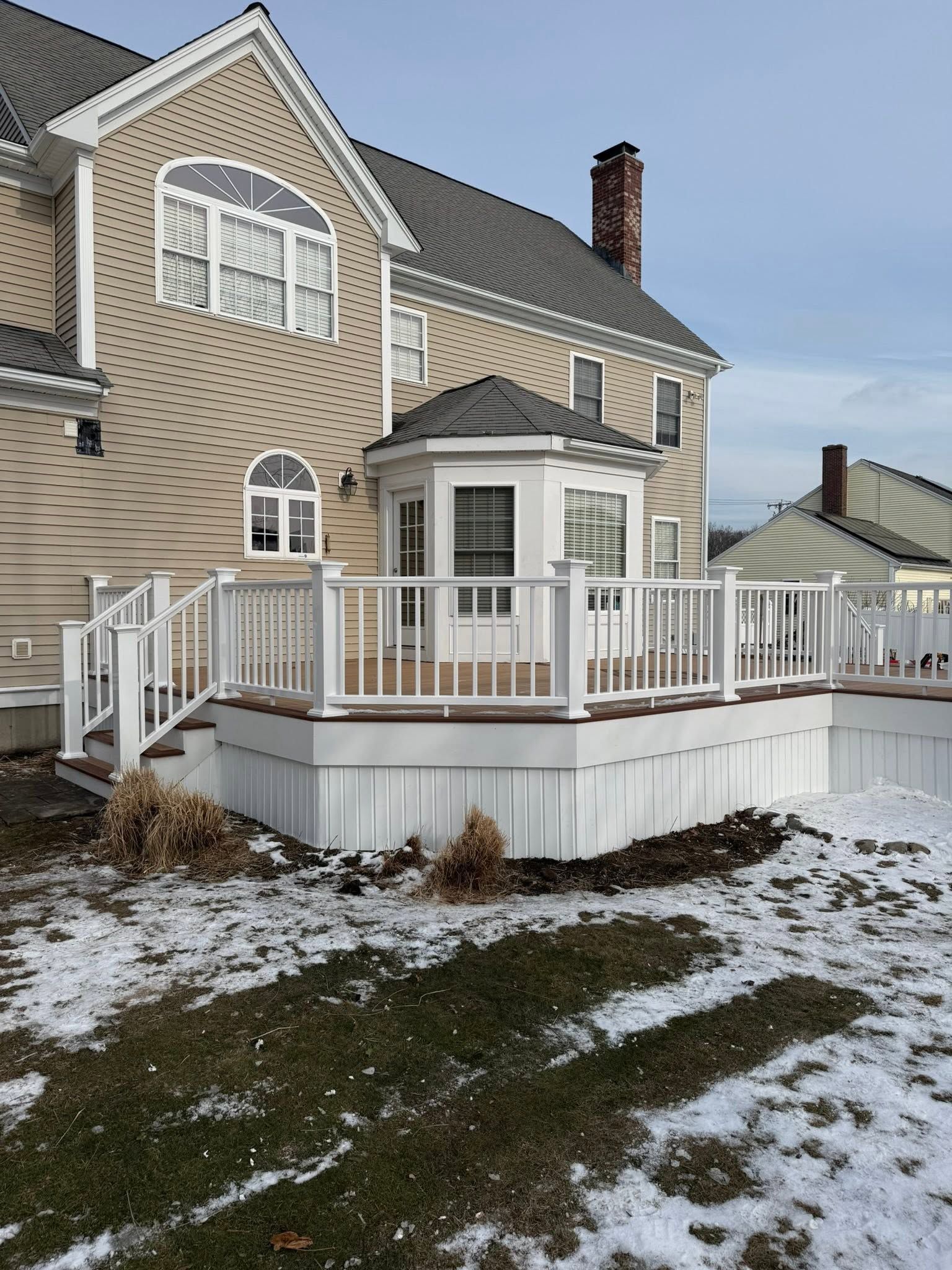 Snowy backyard deck beside beige house with white railing and sliding glass doors
