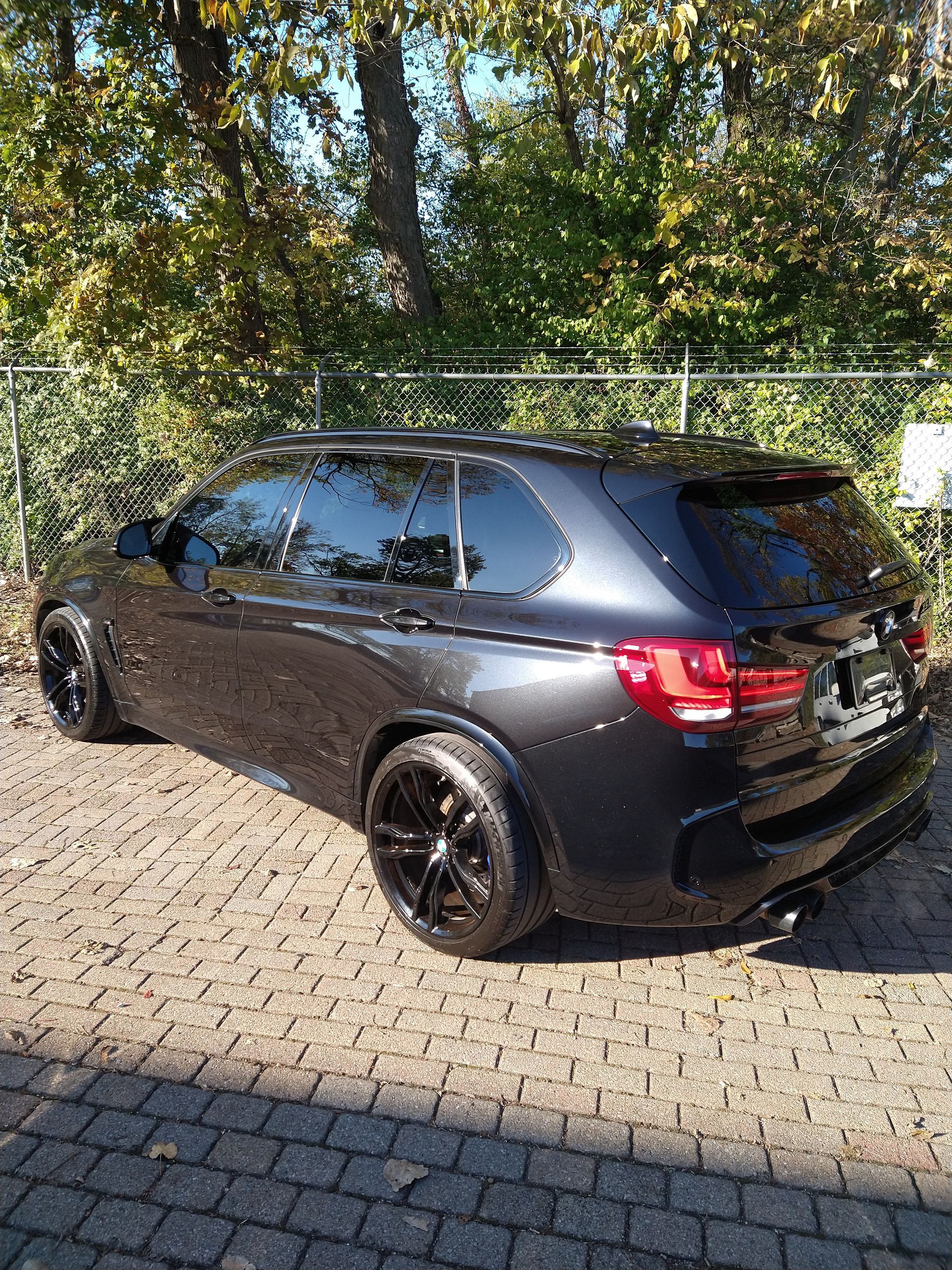 A black bmw x5 m is parked on a brick driveway.