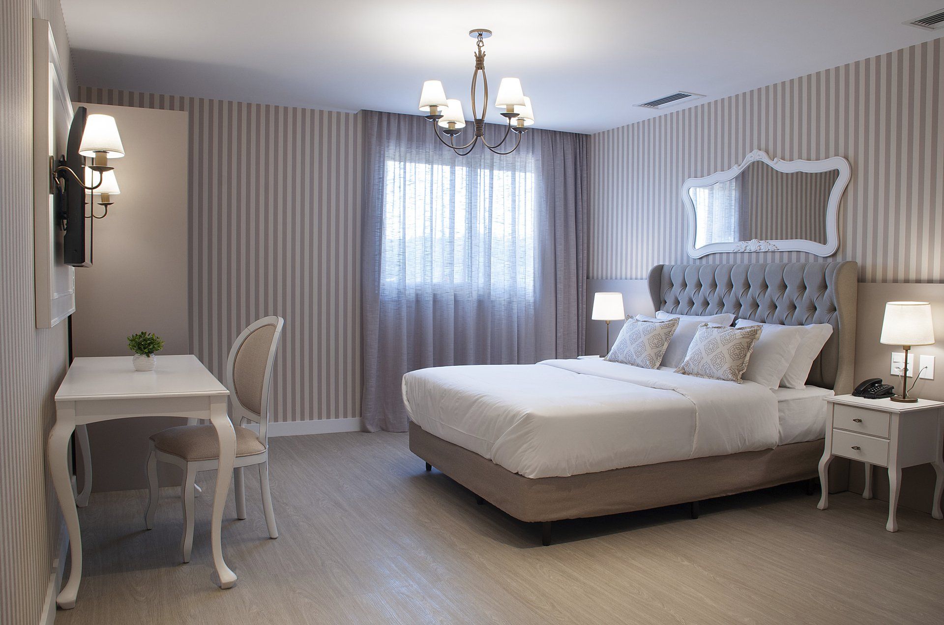 Imagem do quarto do Bella Gramado, com cama de casal, televisor, uma mesa e decoração com cores em tons de cinza.