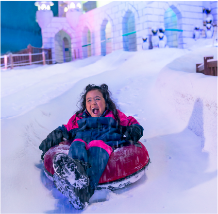 Uma menina está andando em um tubo de neve descendo uma colina coberta de neve.
