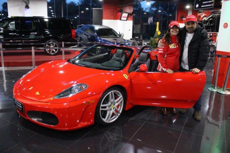 Um homem e uma mulher estão parados ao lado de um carro esportivo vermelho