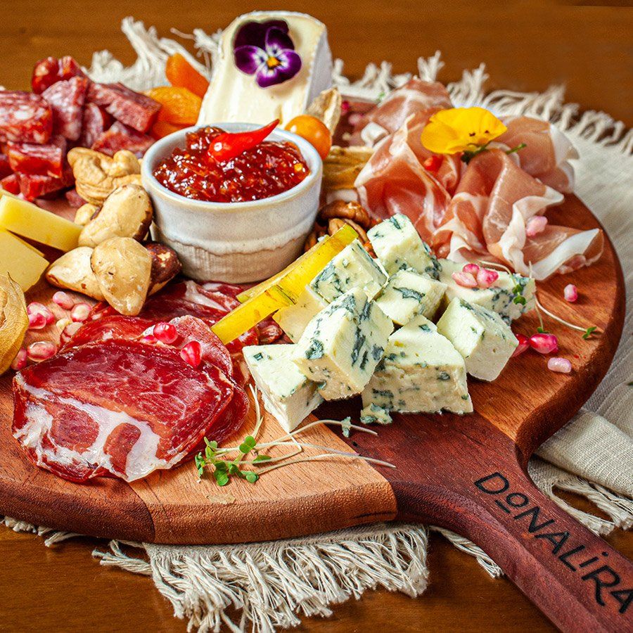 Uma tábua de madeira cheia de carne e queijo sobre uma mesa.