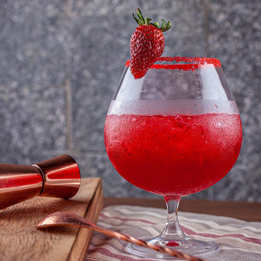 Um copo de líquido vermelho com um morango por cima.