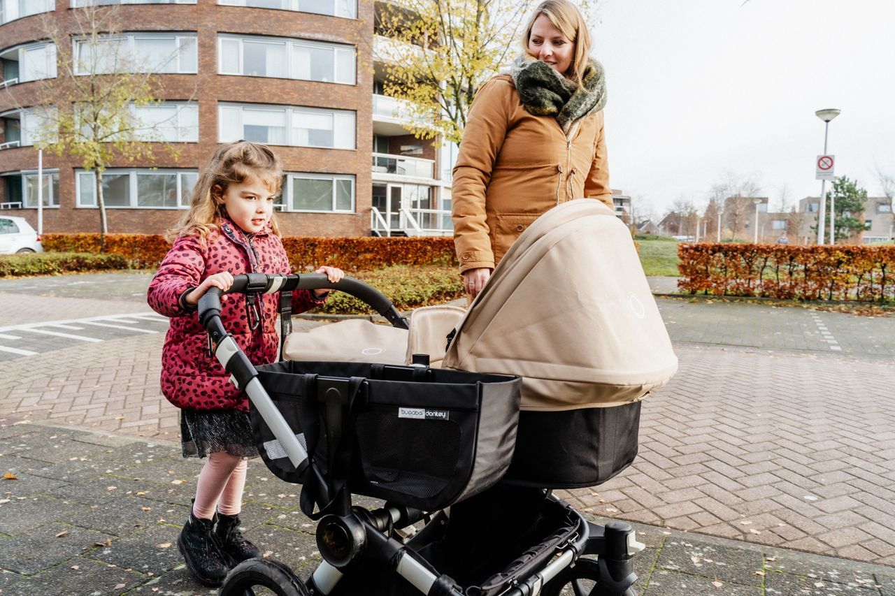 Een vrouw duwt een kinderwagen met een klein meisje ernaast.