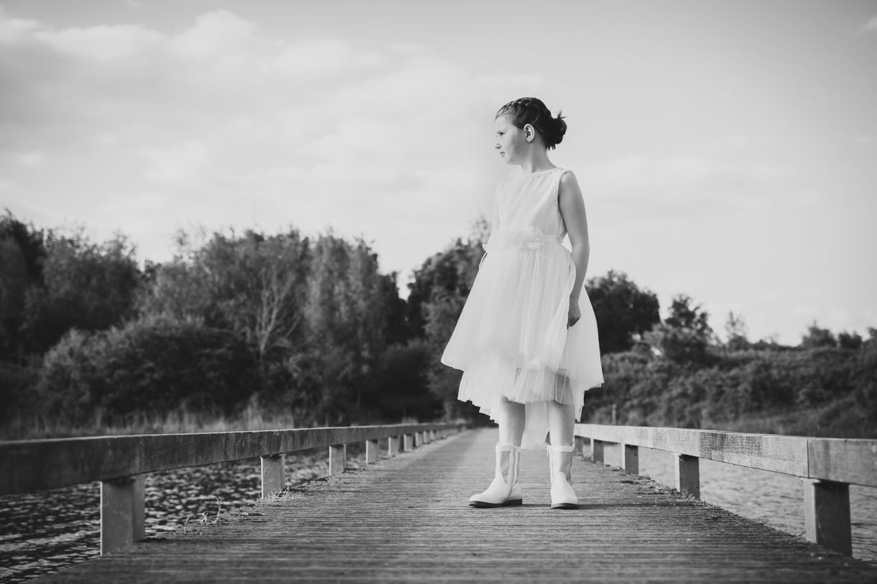 Een klein meisje in een witte jurk staat op een houten brug.