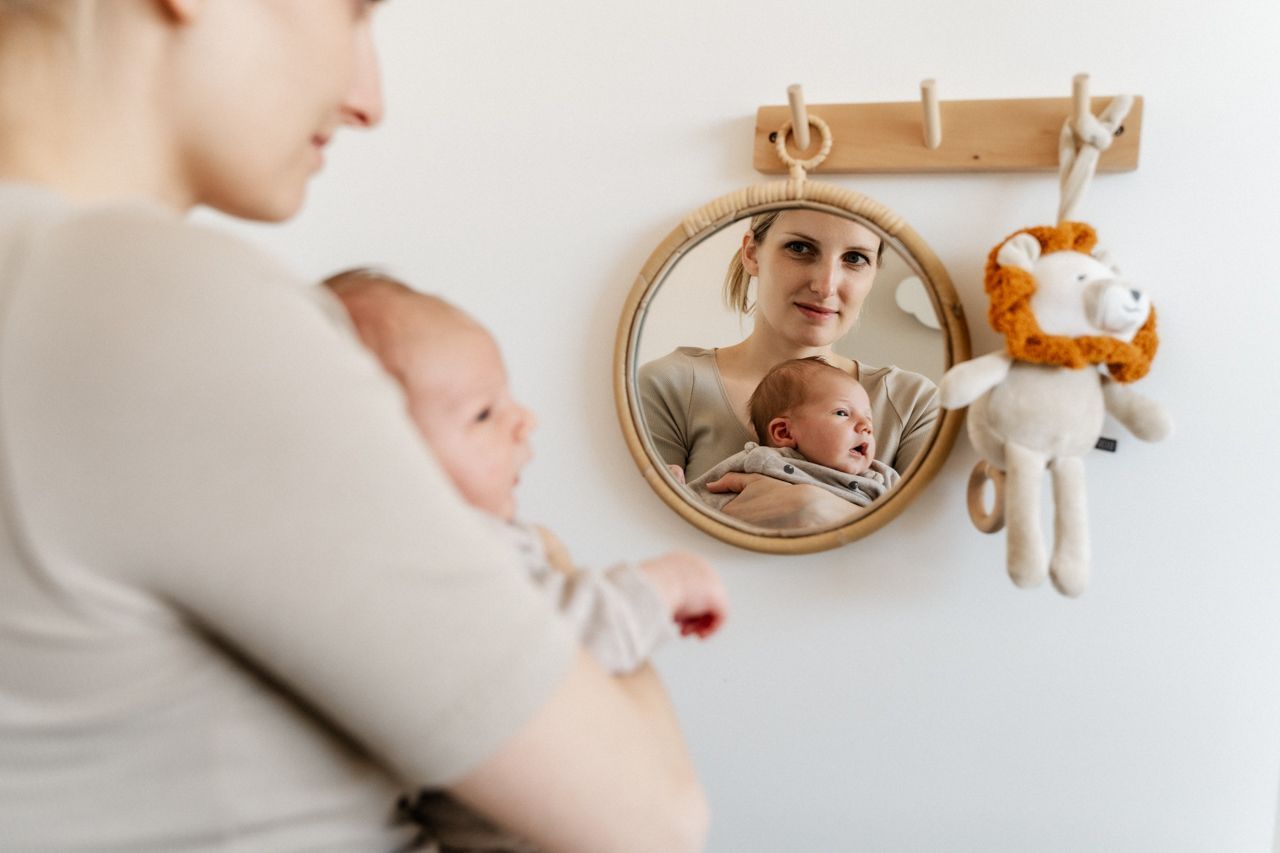 Een vrouw houdt een baby vast en kijkt naar haar spiegelbeeld.