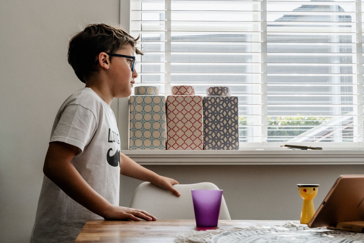 Een jonge jongen met een bril staat aan een tafel en kijkt naar een tablet.