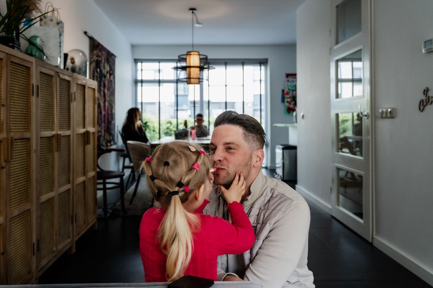 Een klein meisje kust de wang van een man in een woonkamer.