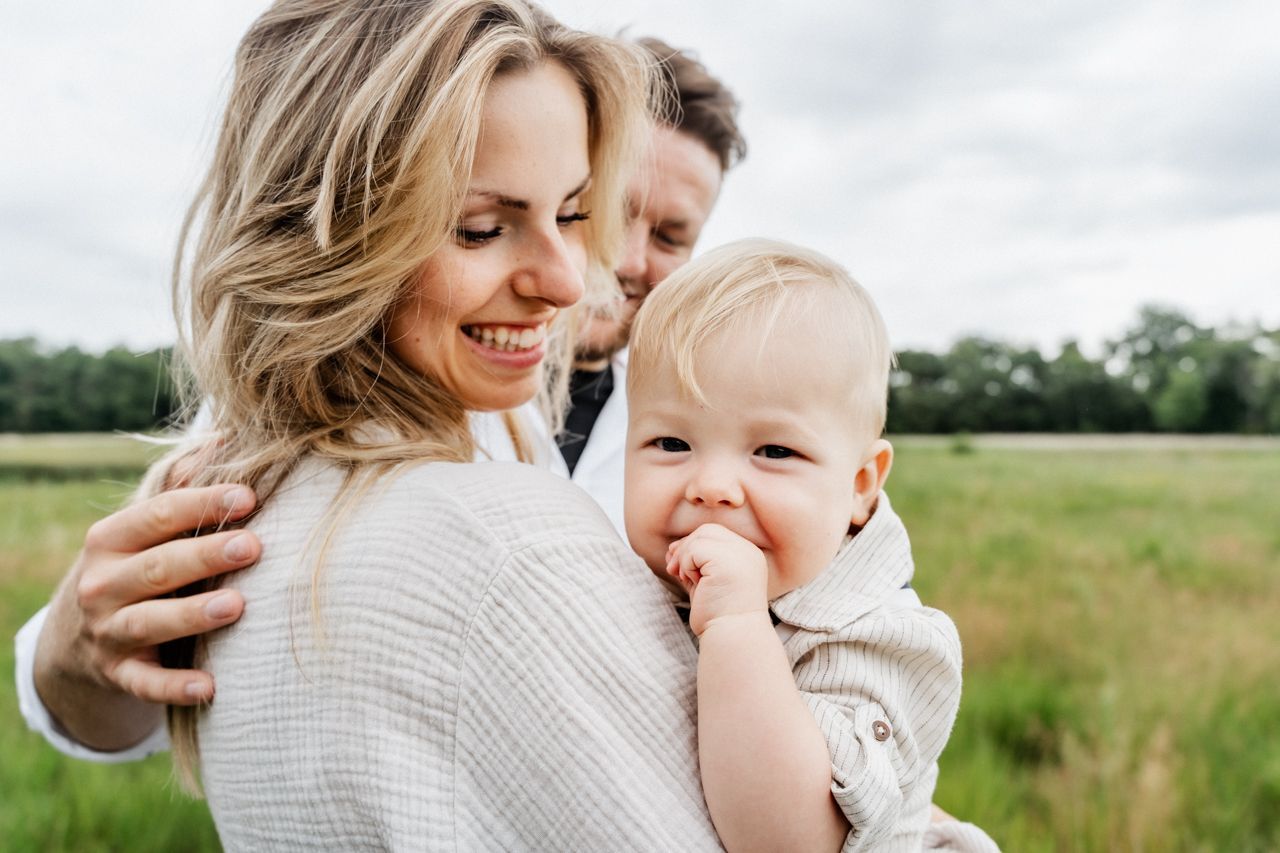 Een vrouw houdt een baby vast in een veld terwijl een man toekijkt.