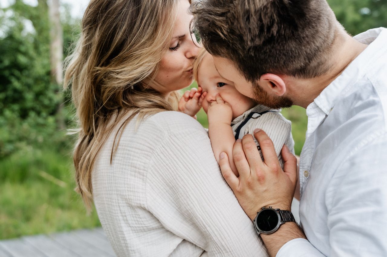 Een man en een vrouw kussen een baby op de wang.
