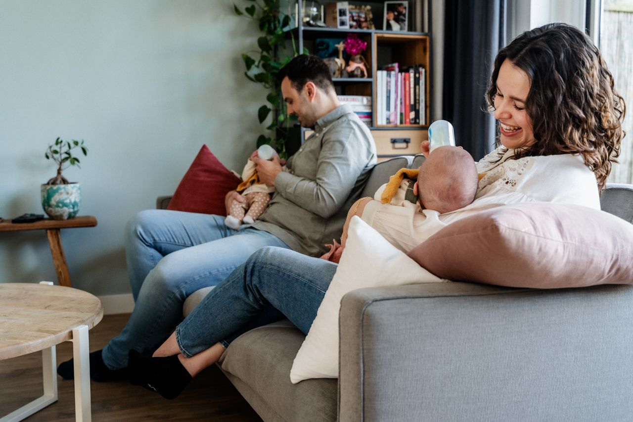 Een man en een vrouw zitten op de bank en houden allebei een baby vast.