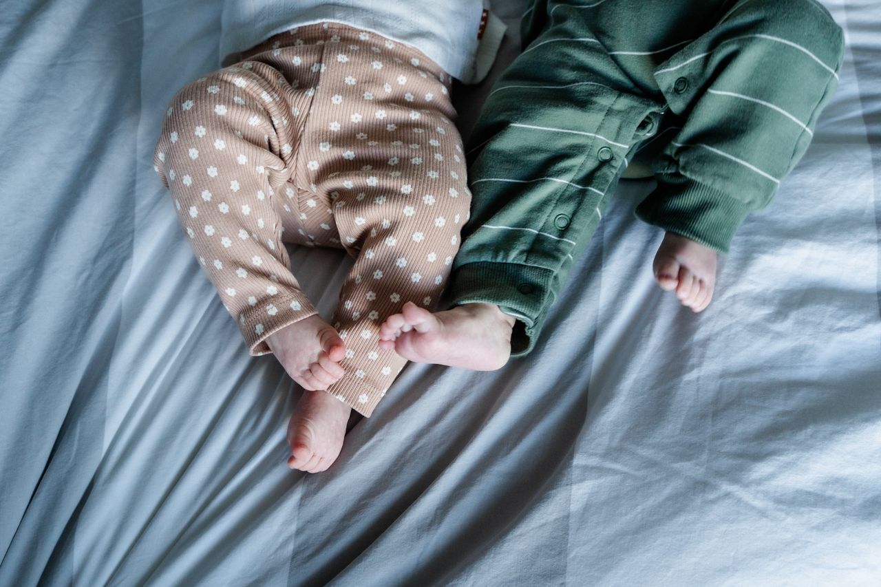 Twee baby's liggen naast elkaar op een bed.
