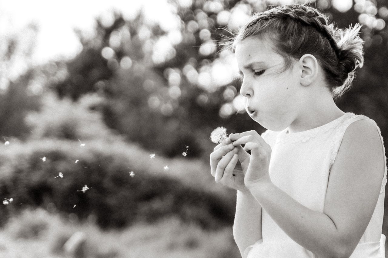 Een klein meisje blaast een paardenbloem op een zwart-witfoto.