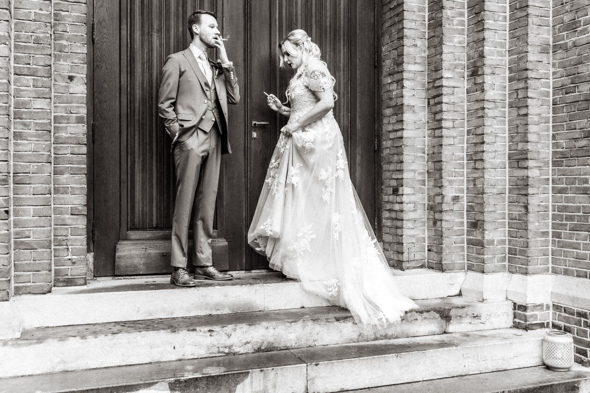 Een bruid en bruidegom staan te roken voor de deuren van de kerk.