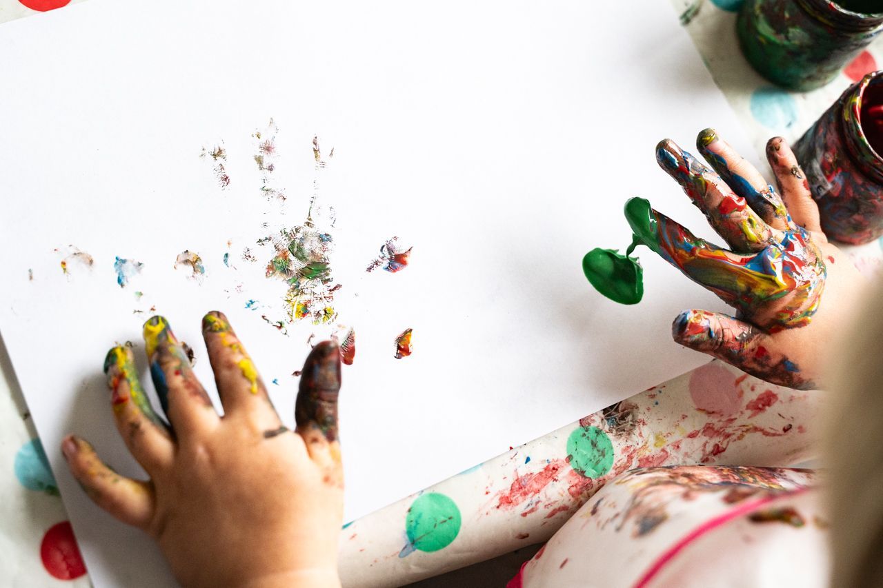 Een kind schildert met zijn handen op een stuk papier.