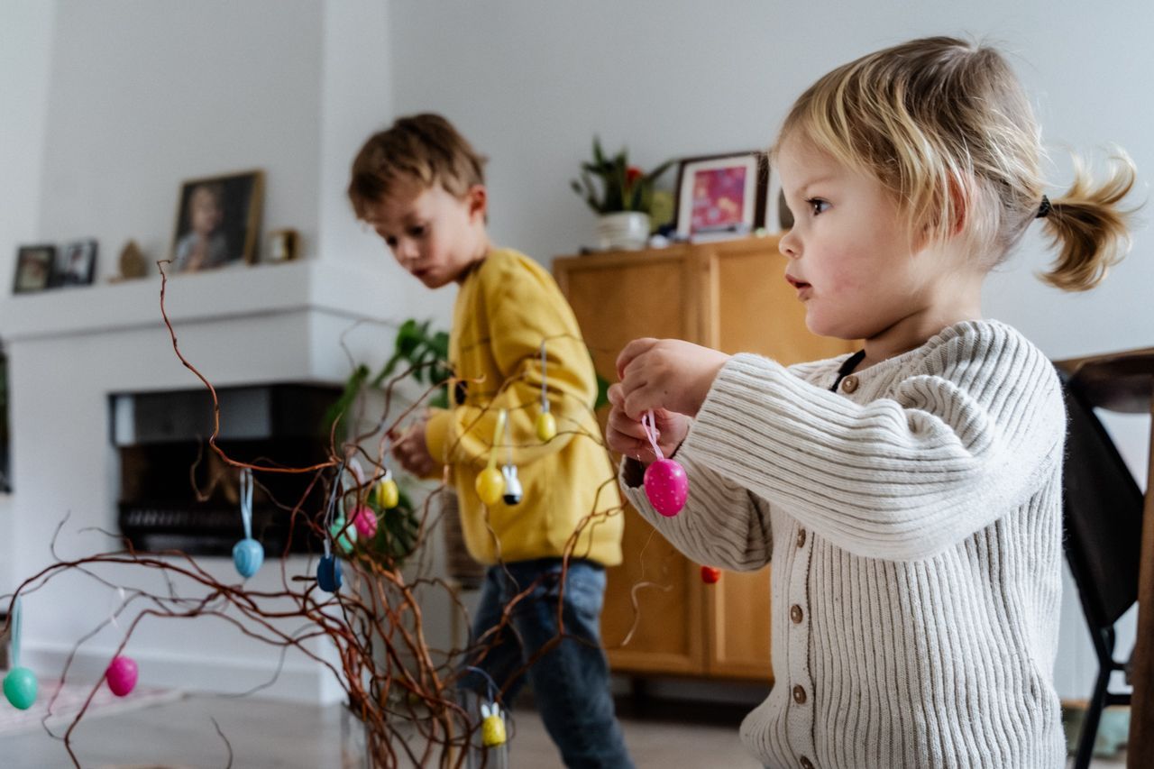 Een jongen en een meisje versieren een boomtak met paaseieren.