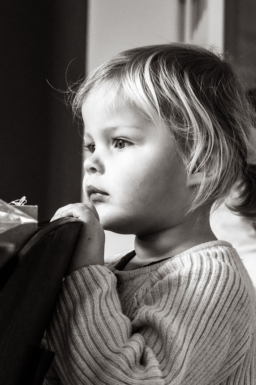 Een zwart-witfoto van een klein meisje dat uit een raam kijkt.