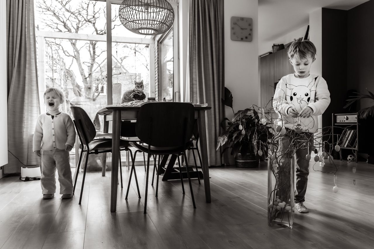 Een zwart-witfoto van twee spelende kinderen in een woonkamer.