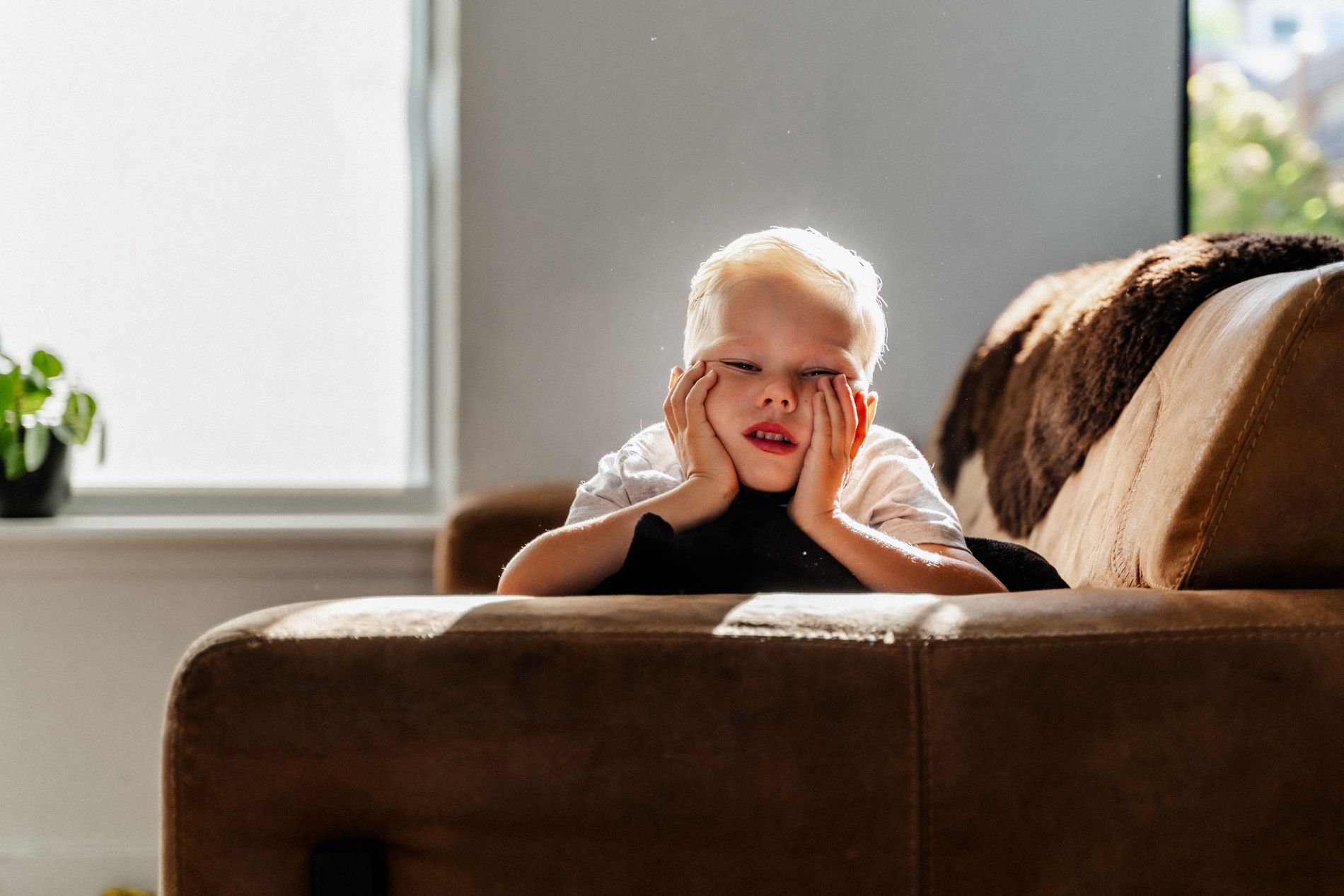 Een jonge jongen ligt op een bank met zijn handen voor zijn gezicht.