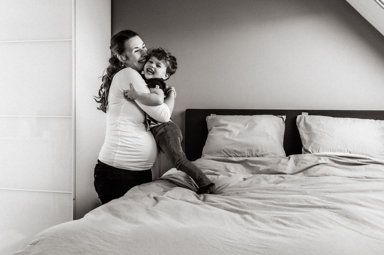Een zwangere vrouw knuffelt een kind op bed.