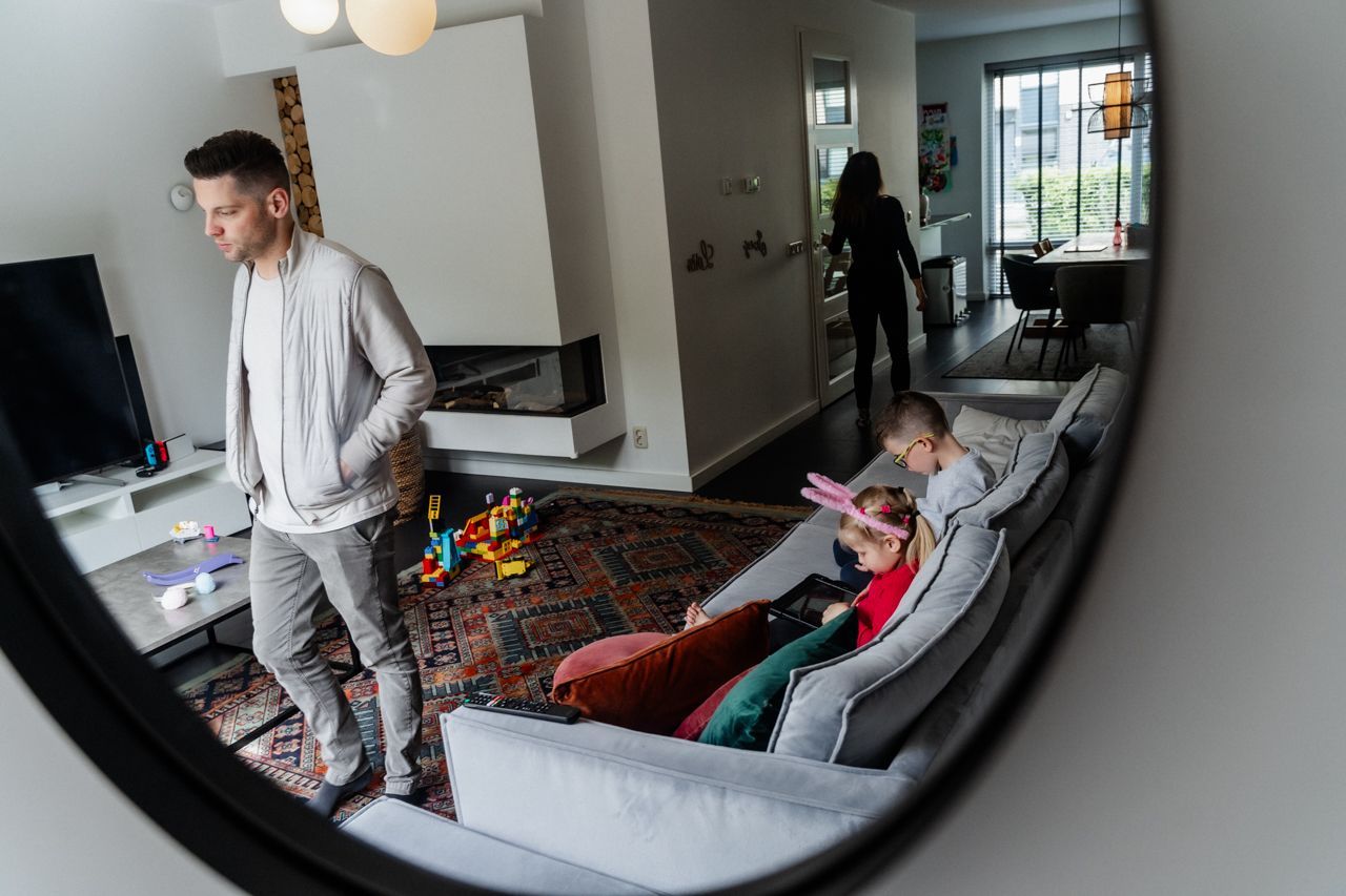 Een man staat in een woonkamer naast een bank en een spiegel.