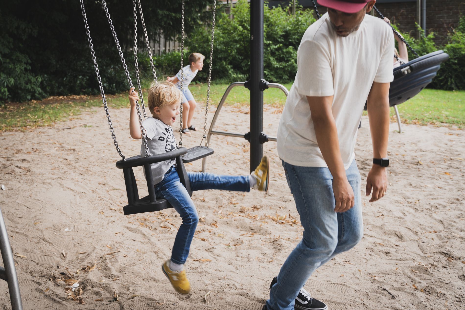 Een man speelt met een kind op een schommel in een speeltuin.