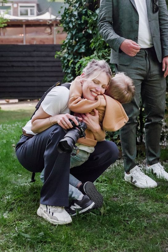 Een vrouw knielt neer en houdt een baby en een camera vast.