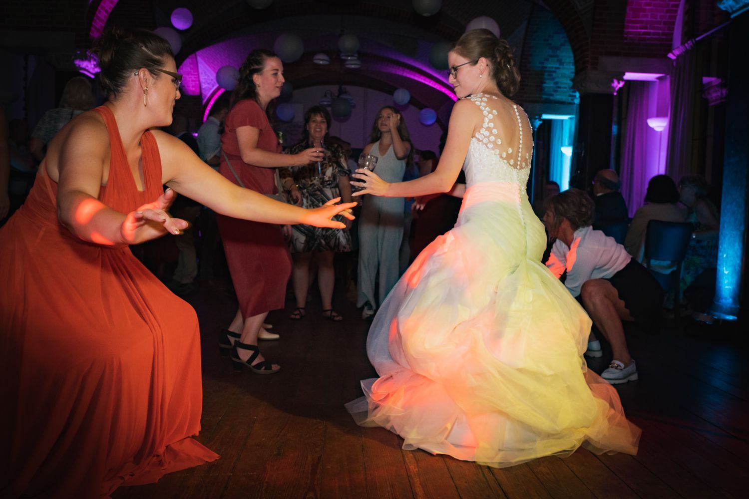 Een bruid en haar bruidsmeisjes dansen op een dansvloer tijdens een huwelijksreceptie.
