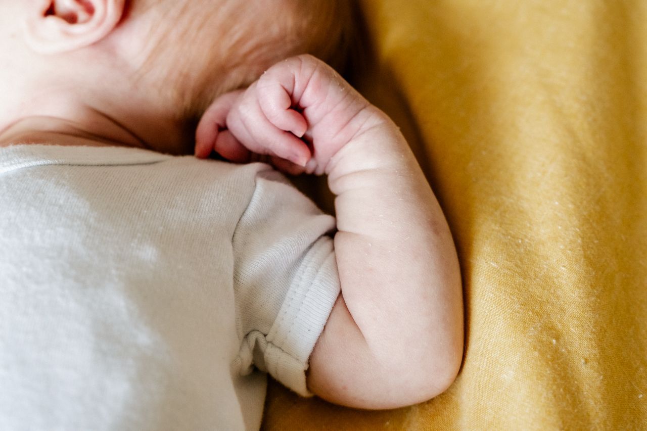 Een baby slaapt op een gele deken met zijn hand op zijn oor.