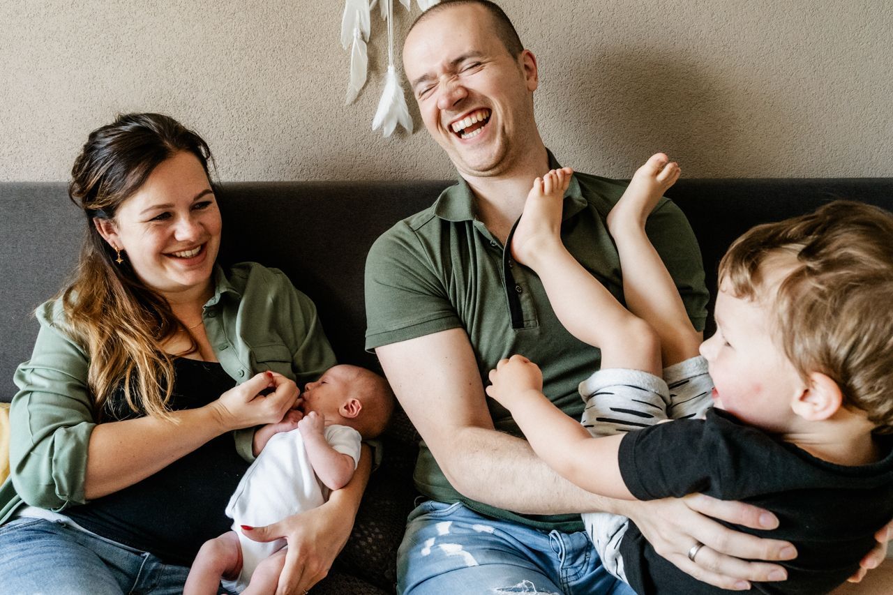 Een gezin zit op een bed met twee kinderen en een pasgeboren baby.