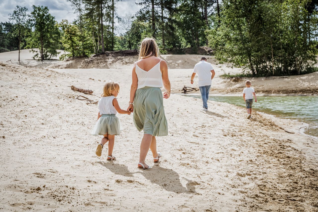 Een vrouw en twee kinderen lopen hand in hand over het strand.