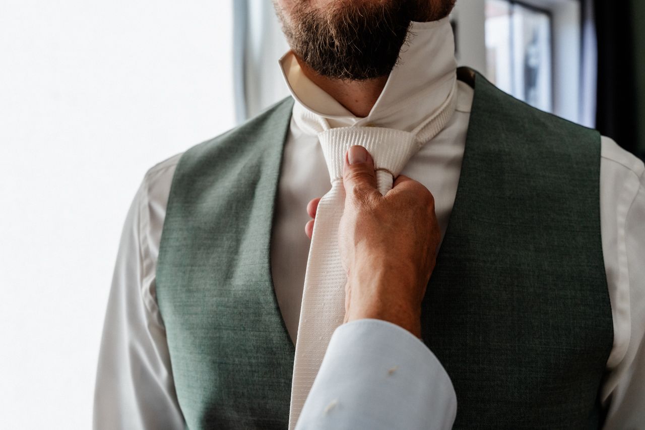 Een man met een baard maakt zich klaar voor zijn bruiloft door zijn stropdas te knopen.