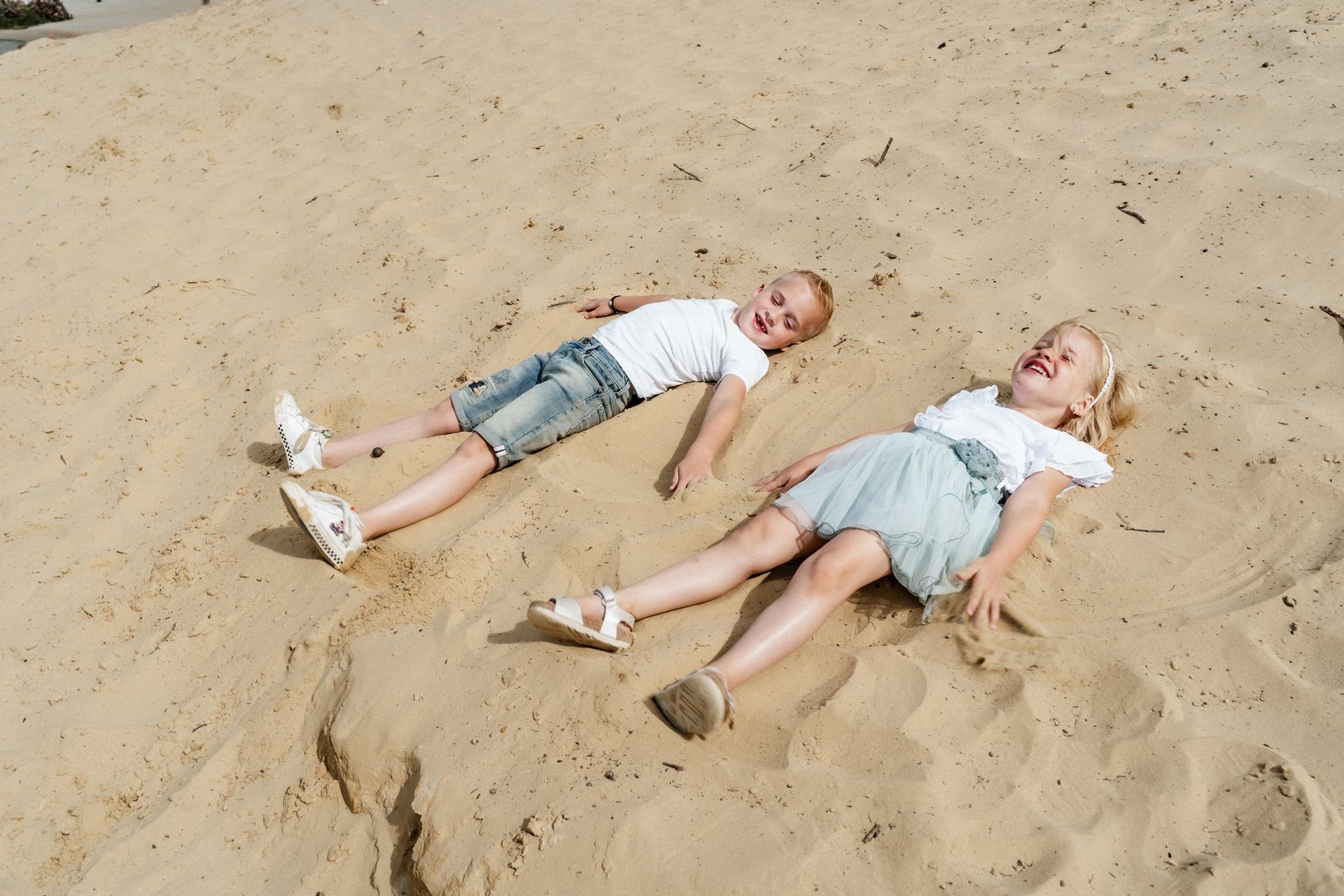 Een jongen en een meisje liggen in het zand op het strand.