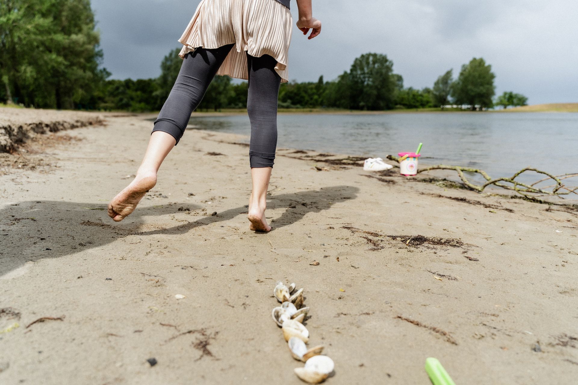 Een vrouw loopt blootsvoets op een strand naast een watermassa.