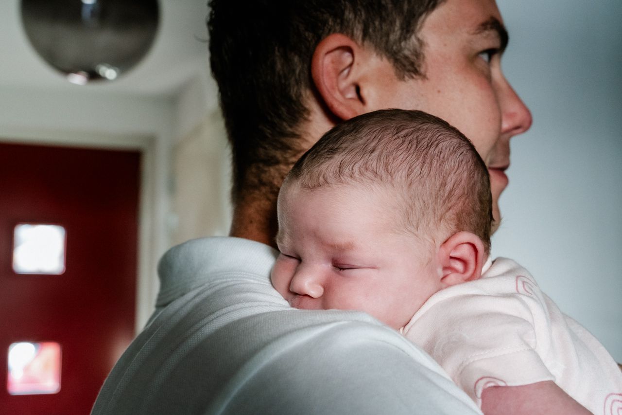 Een man houdt een baby over zijn schouder.