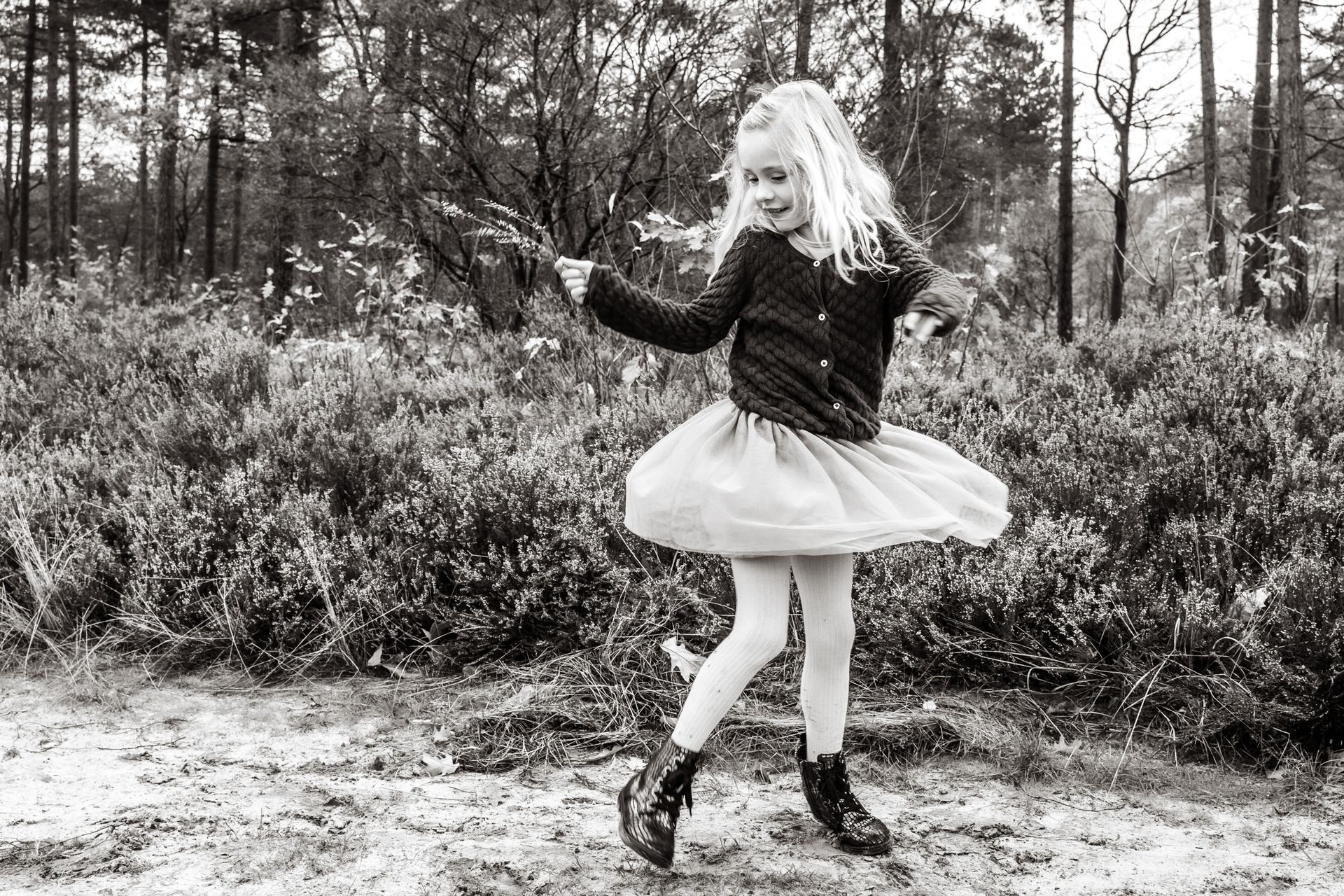Een klein meisje danst in het bos op een zwart-witfoto.
