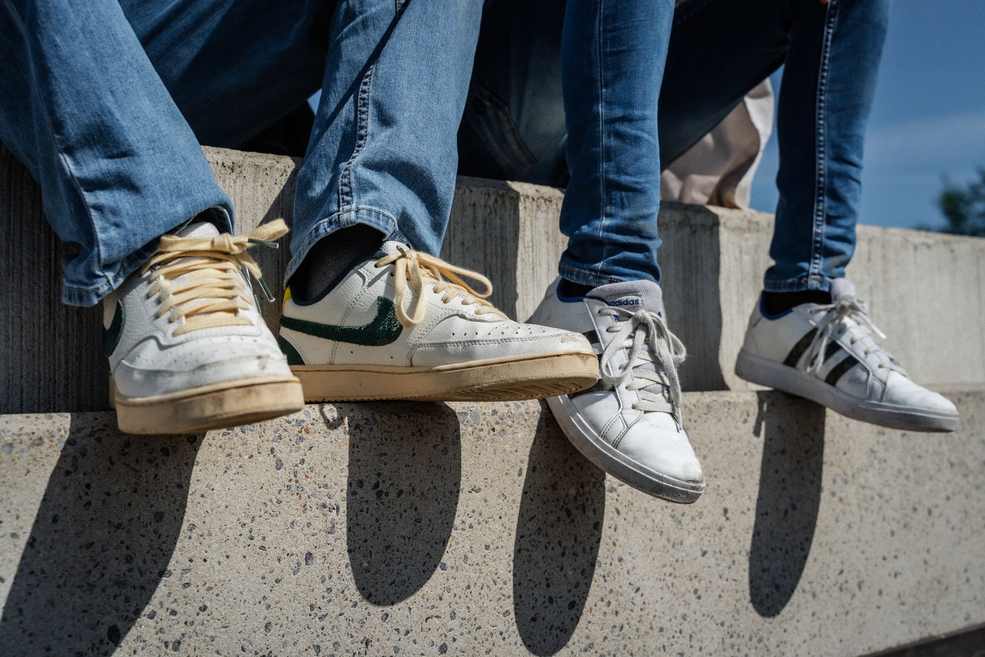 Twee mensen zitten op een betonnen muur en dragen sneakers.