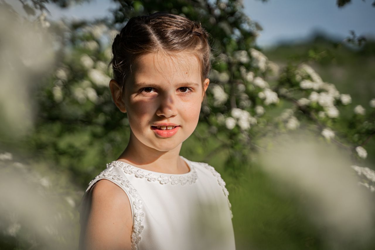 Een klein meisje in een witte jurk staat voor een boom.