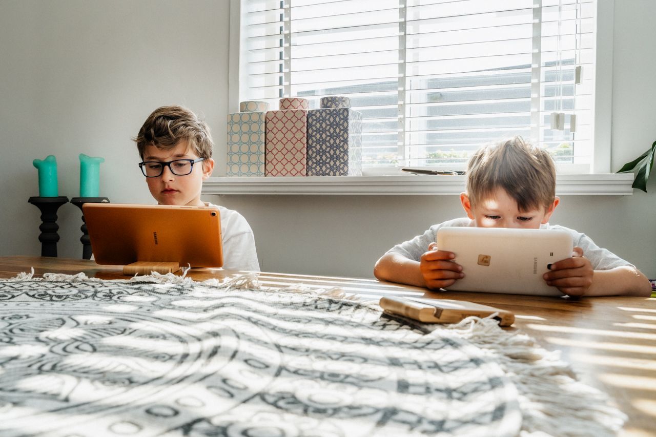 Twee jonge jongens zitten aan een tafel en kijken naar een tablet.