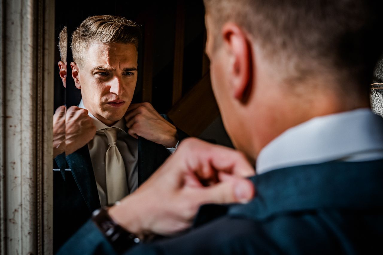 Een bruidegom checkt zijn kleding in de spiegel.