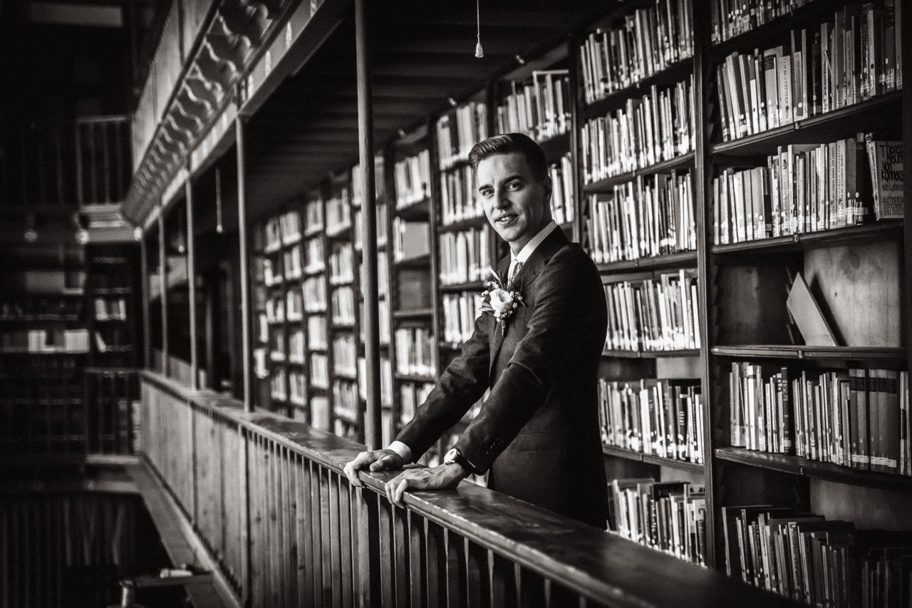 Een zwart-witfoto waarbij de bruidegom in een oude bibliotheek staat.
