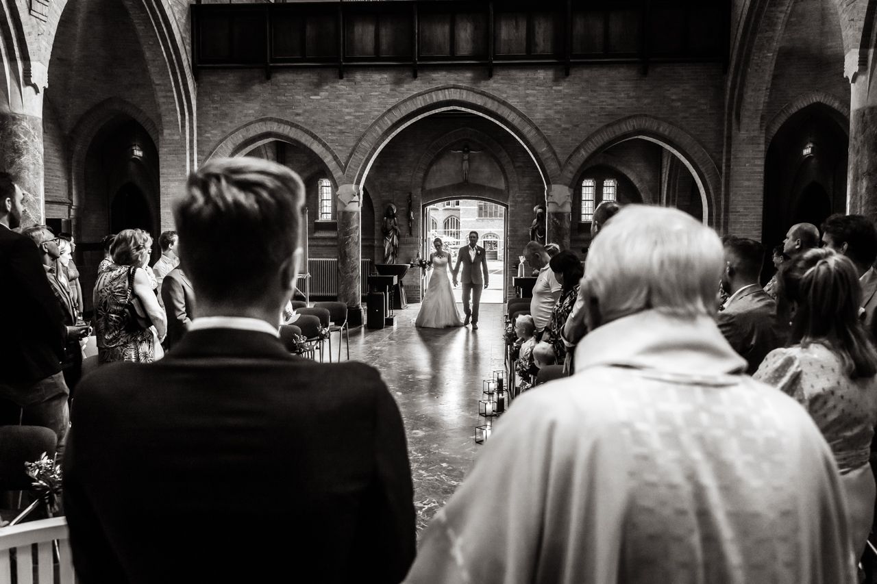 Een zwart-witfoto van een bruid en bruidegom die door het gangpad van een kerk lopen.