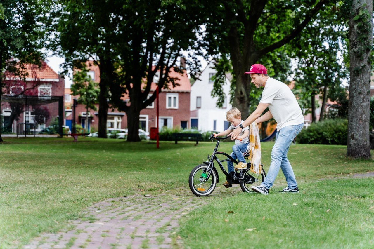 Een man leert een kind fietsen in een park.