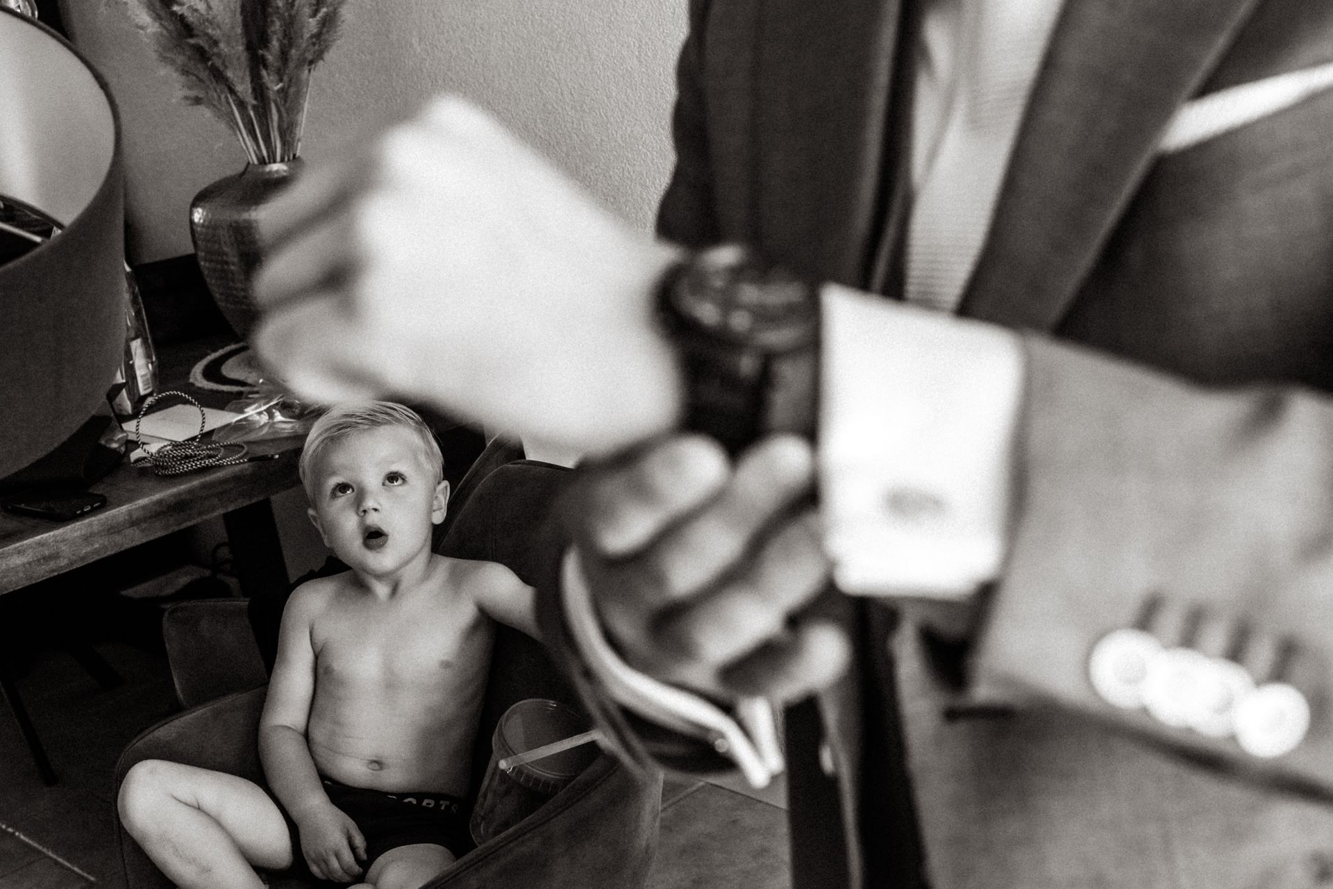 Een man in pak trekt zijn stropdas recht, terwijl een jongetje op de grond zit.