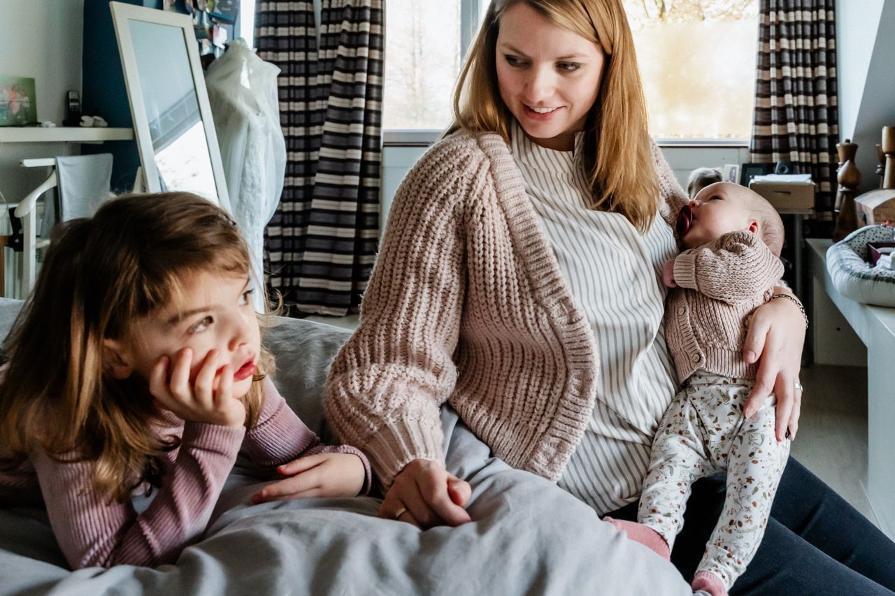Een vrouw zit op een bed en houdt een baby en twee kleine meisjes vast.