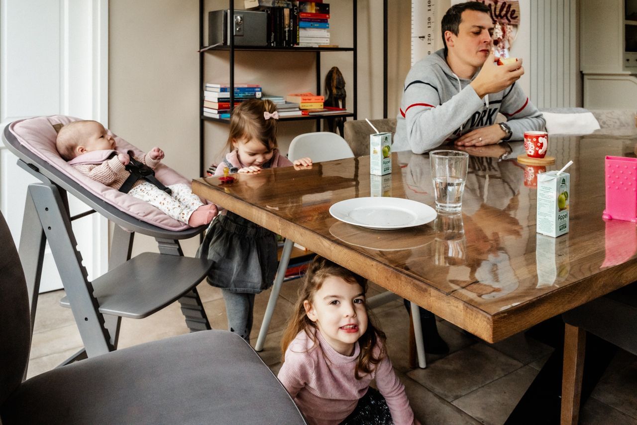 Een man zit aan een tafel met twee kleine meisjes en een baby in een kinderstoel.