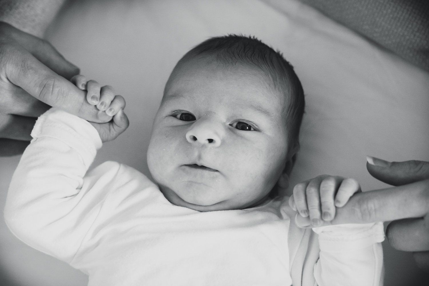 Een zwart-witfoto van een pasgeboren baby die de vinger van een vrouw vasthoudt.
