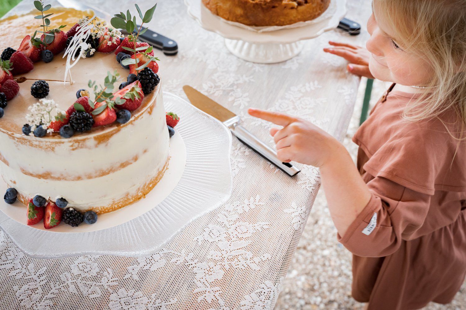 Een klein meisje wijst naar een taart op een tafel.